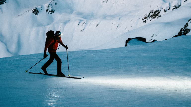 Ein Skifahrer mit einer starken und guten Lampe auf einem Berg in der Nacht.