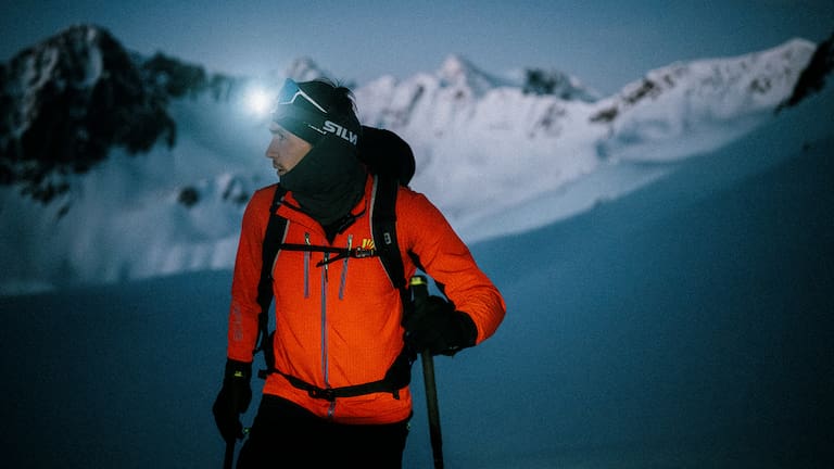 Ein Mann geht im Schnee und Skiausrüstung in der Nacht mit einer Stirnlampe skifahren.