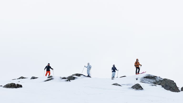 Vier Skifahrer stehen auf einen Gipfel und tragen robuste und moderne Outdoor-Kleidung.