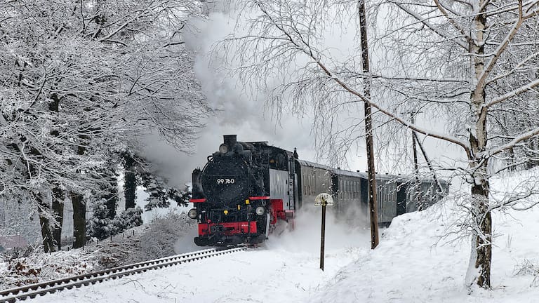 Eine Bahn auf Schienen durch einen verschneiten Wald in rot und schwarz.