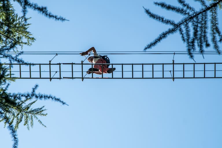 Person im Klettersteigset auf einer Drahtseilleiter von unten mit blauem Himmel im Hintergrund