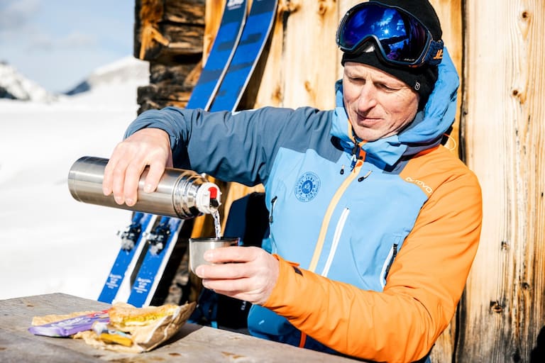 Mann trinkt Tee vor Hütte im Winter