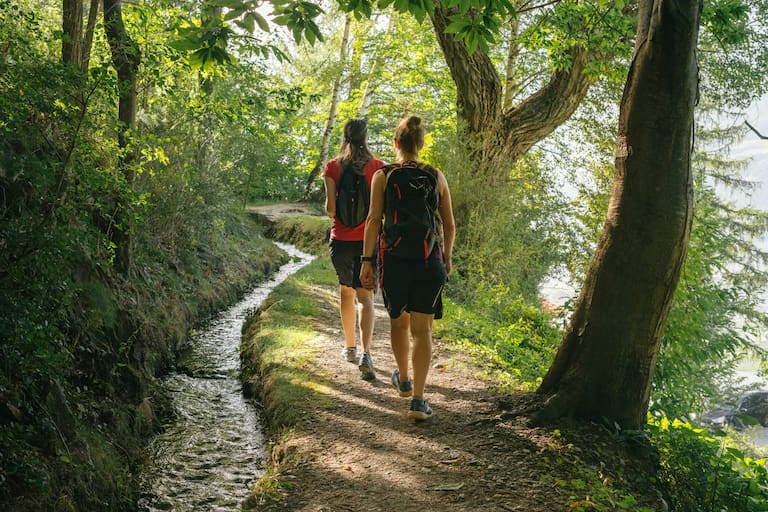 zwei Wanderinnen gehend entlang eines Waalweges in Südritol im Wald