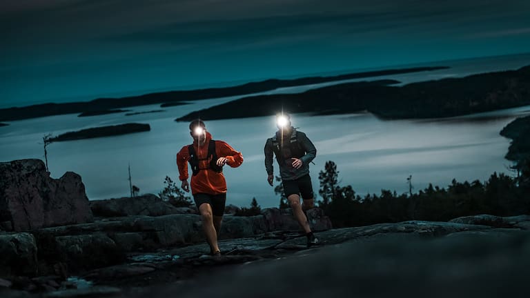 Zwei Trailrunner in der Nacht mit Stirnlampen.