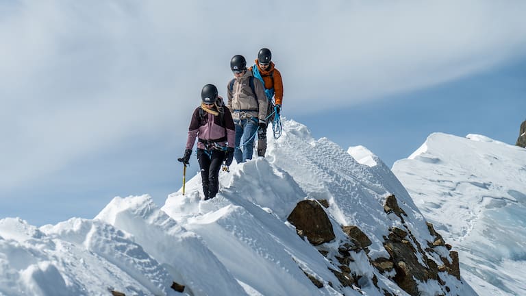 Drei Menschen die einen schneebedeckten Berg besteigen.