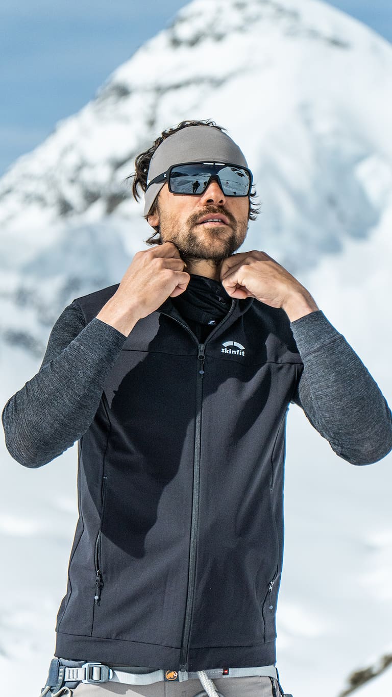Ein Mann auf dem schneebedeckten Berg bei einer Hochtour in seinem skinfit Outfit und Brille